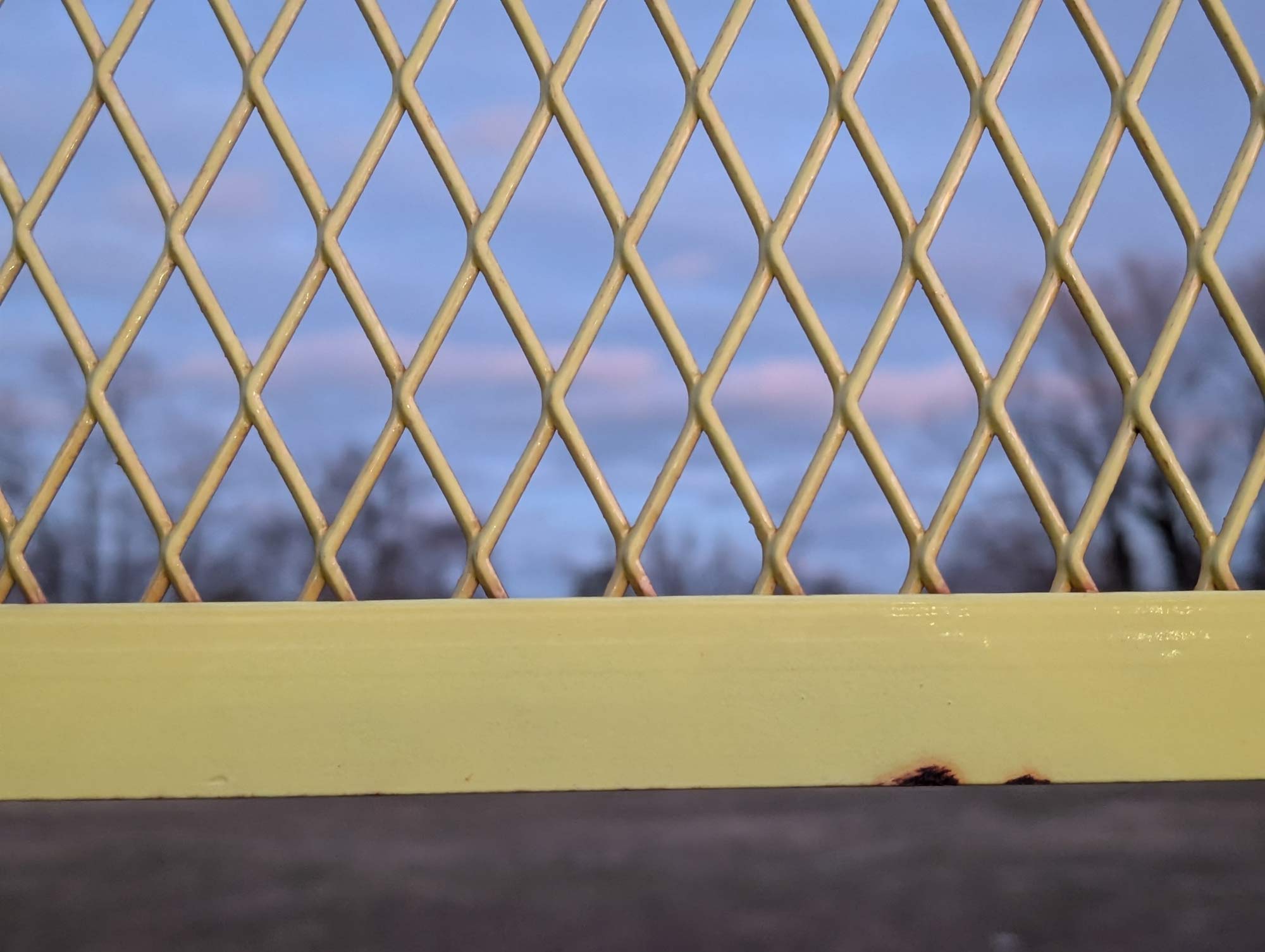 An empty yellow steel mesh section of a first base foul pole