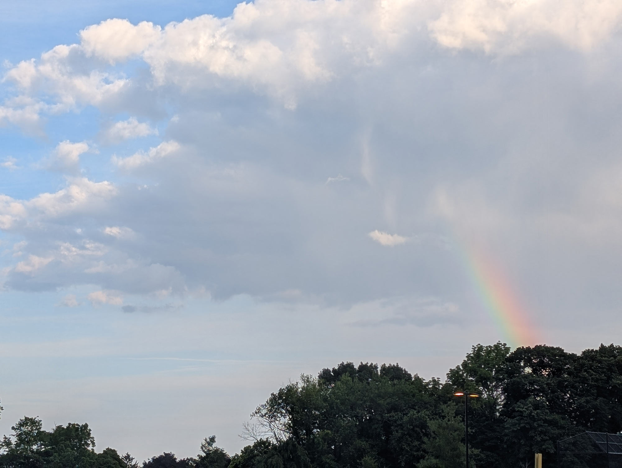 The end of a rainbow extending out of a white cloud in a clear blue sky
