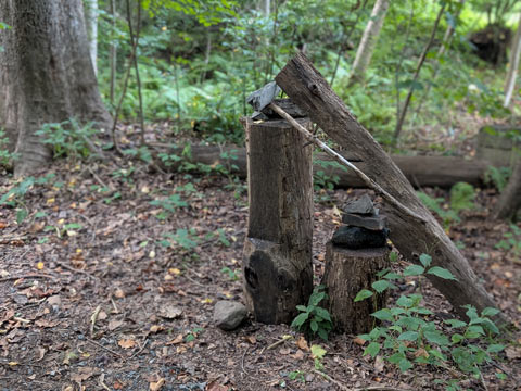 An art assemblage found in the woods. A decaying log standing upright, with a smaller piece of stump next to it. A small pile of stones stacked atop each