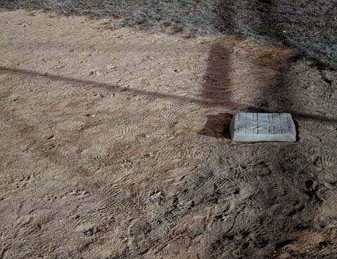 A first base bag bathed in the light of a distant flood light, surrounded by footprints