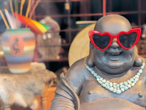 A statue of a smiling Buddah wearing a pair of red heart-shaped sun glasses