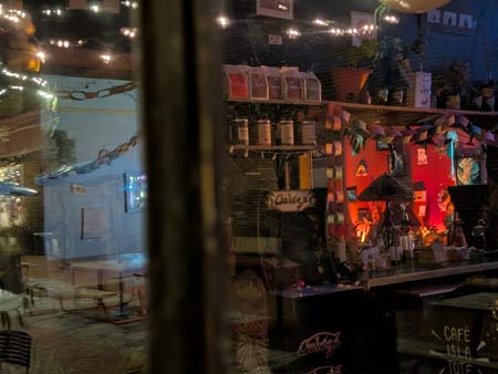 looking through the window into a coffee shop, with the reflection of a table and chairs just outside.
