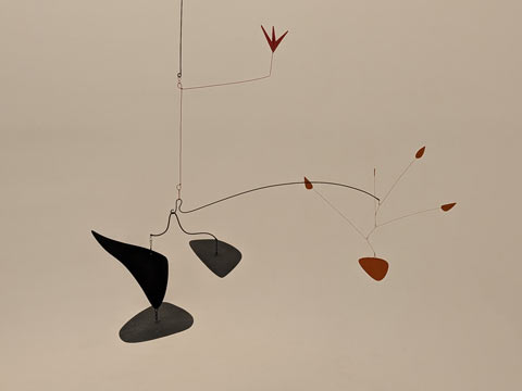 An mobile (by Alexander Calder) balancing large black and small red organic shapes on opposing sides, with one red bird shape balanced above