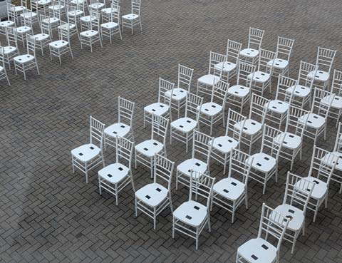 Empty white folding chairs lined up in two groups of columns and rows on a paver patio