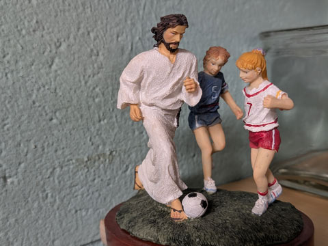 A ceramic of Jesus dribbling a soccer ball with two children chasing after him