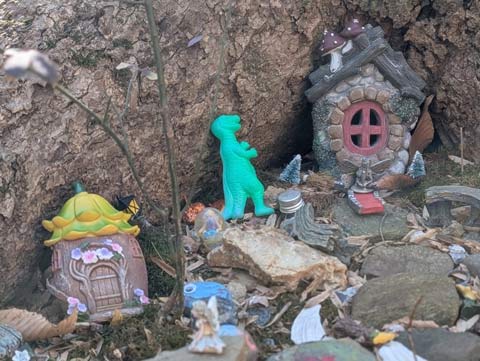 Plastice toys arranged at the foot of a large Tulip Poplar tree to look like a place where fairies live. And a green Tyranosaurus Rex