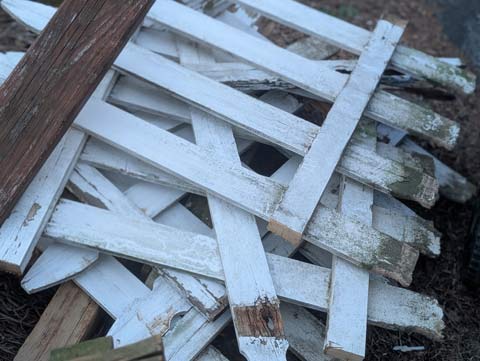 Sections of old white picket fence, piled up waiting to be picked up as trash
