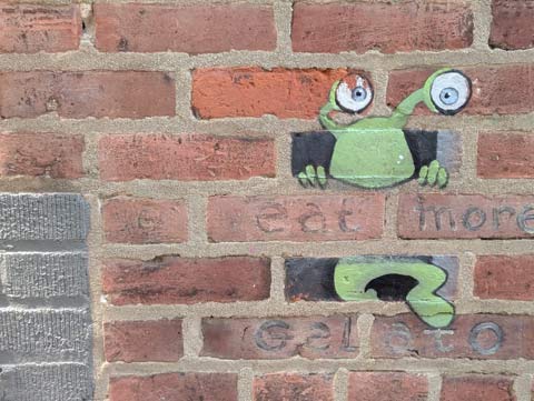 grafitti illustration on a brick wall, including a green alien with eyes on stalks, along with the words "Eat more gelato "