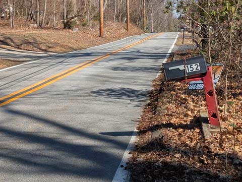 A mail box attached to an upturned bench, which is being used as a post, by a bungee cord. The bench is painted red, and has two heart shapes cut out on either side.
