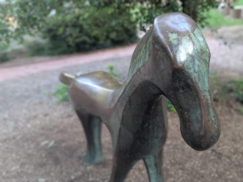 A bronze statue in the shape of a horse. It is very smooth, and while old, it only has a few areas that have a patina due to it's location at a school where it is constantly touched and sat upon by children