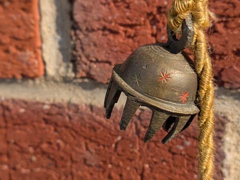Tibetan meditation bell hanging from a thin golden rope in front of a brick wall