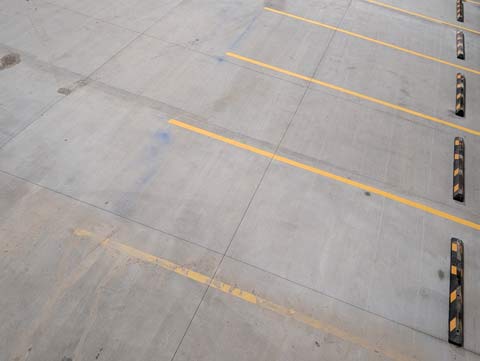 A view from above of an empty cement floored parking garage floor, with yellow lines and black and yellow parking stops making a vertical dashed line