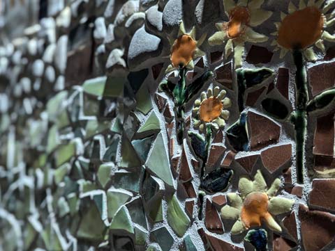 Close up of section of a wall mosaic that includes daises in the forefront