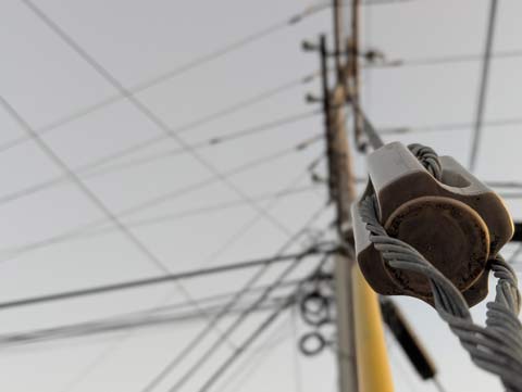 A ceramic metal wire cable connector, connecting a stability cable attached to a utility pole, to the end of another stability cable attached to the ground