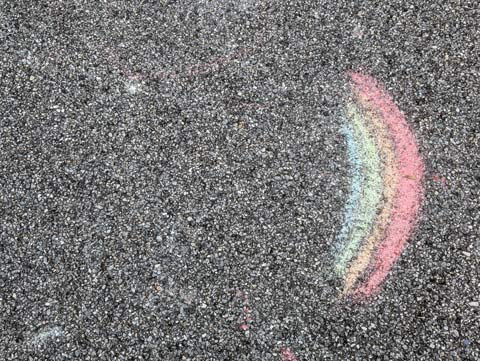 A rainbow drawn in chalk on the asphalt ground of a playground