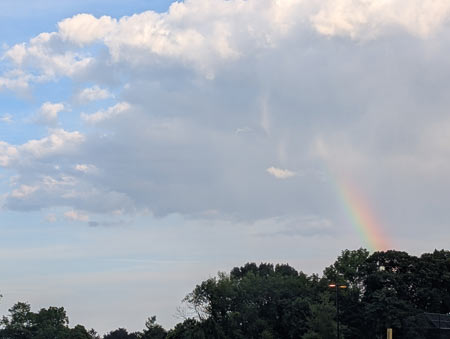 The end of a rainbow extending out of a white cloud in a clear blue sky