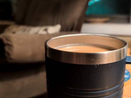 A steaming cup of coffee in a blue metal mug sitting on an end table