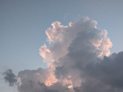 Sunlight filtering through the edges of a cumulus cloud, tinging it with soft shades of blue, orange and pink