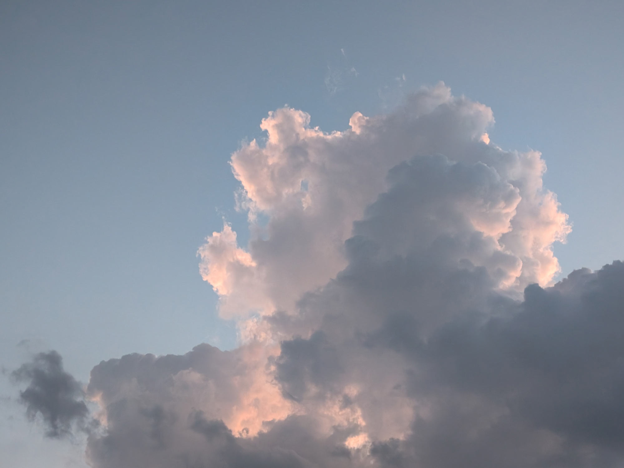 Sunlight filtering through the edges of a cumulus cloud, tinging it with soft shades of blue, orange and pink